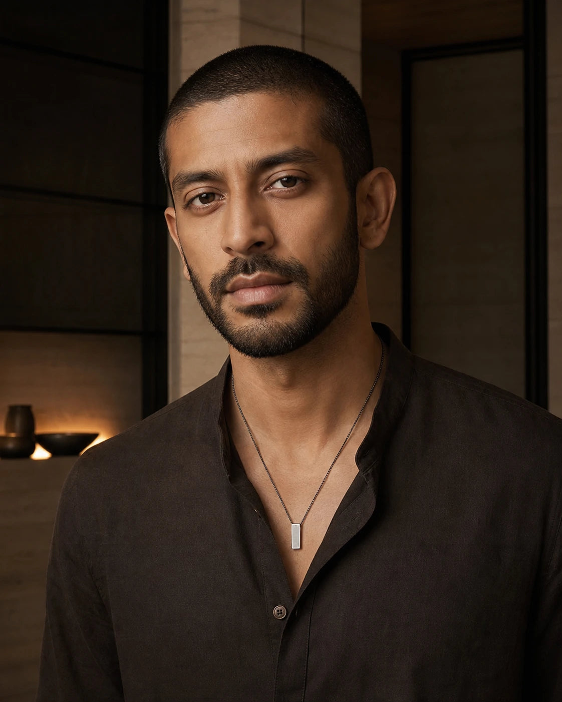 South Asian male model wearing the DARENZ Footnote Pendant in brushed steel, styled in a warm limestone residence