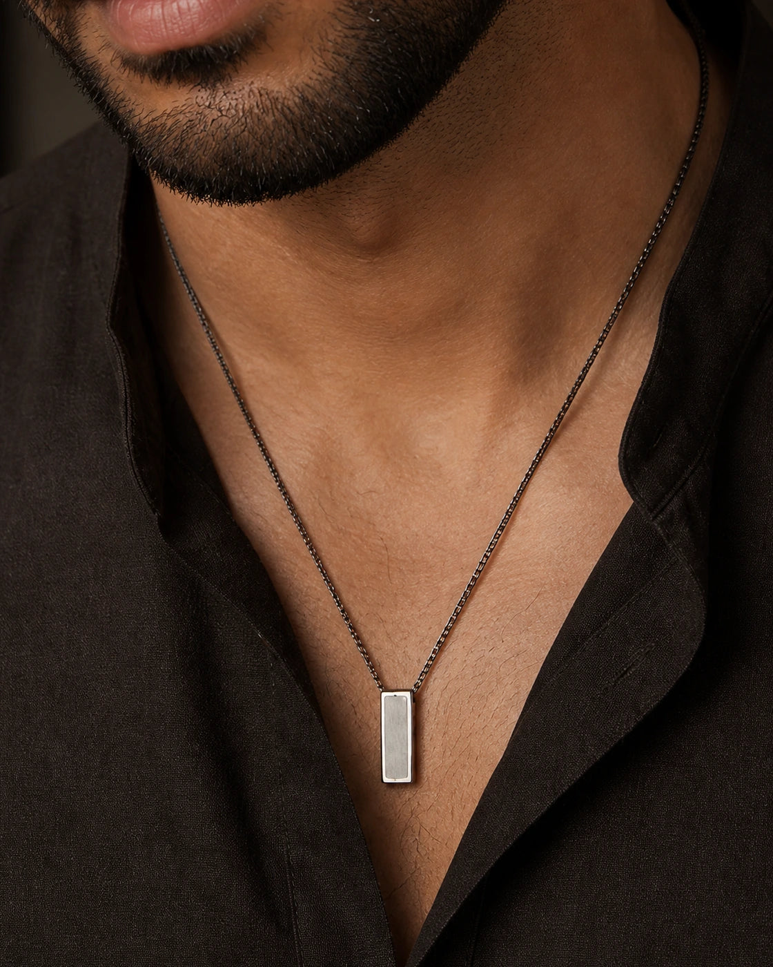 Macro photograph of the DARENZ Footnote Pendant, revealing the beveled rectangular face, brushed grain and recessed corner notch
