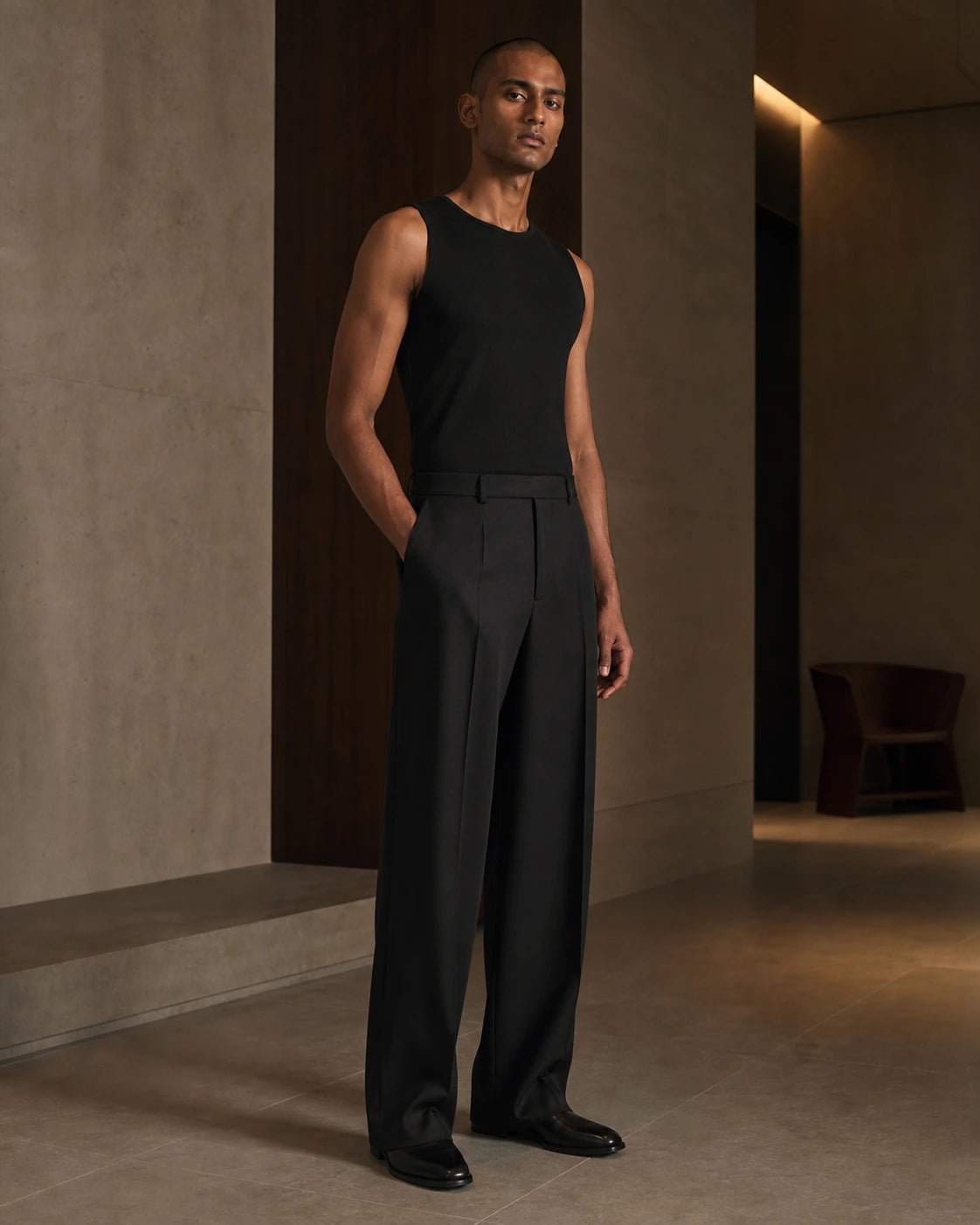 South Asian male model wearing the DARENZ Long Form Loose Tailored Trousers in Ink, full-length front view in a warm limestone residence
