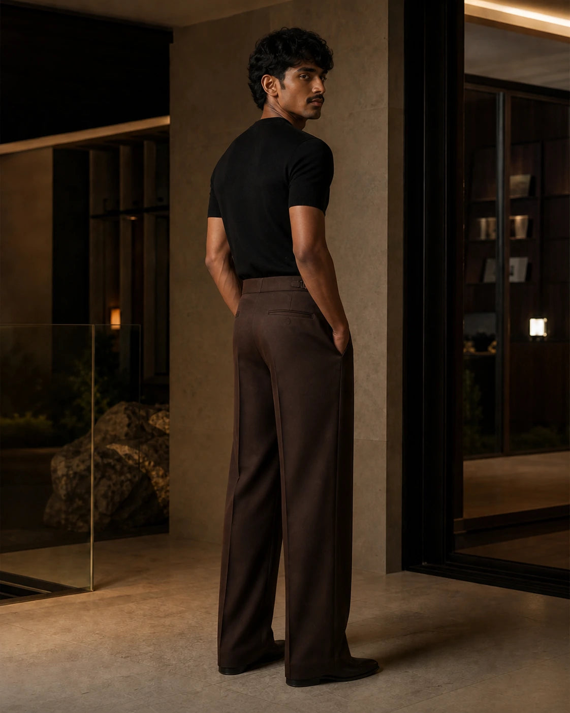 Side and back view of the Umber DARENZ Long Form Loose Tailored Trousers on its assigned model near smoked glass
