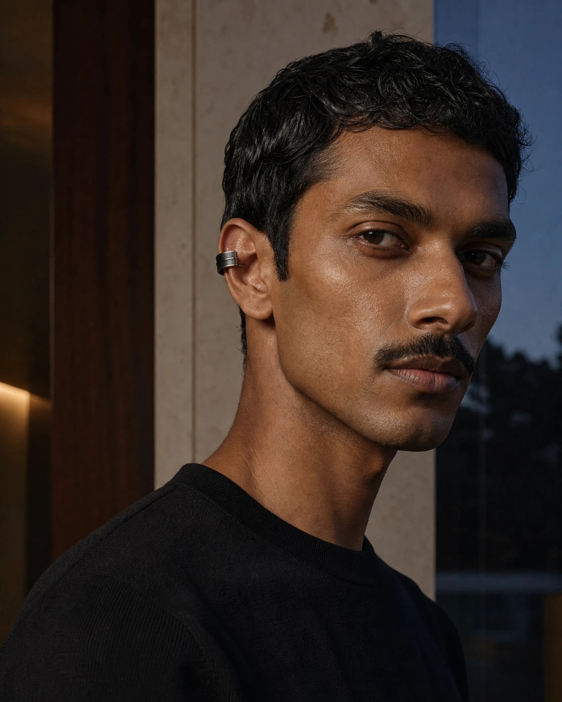 South Asian male model wearing the DARENZ Margin Ear Cuff in blackened steel, styled in a warm limestone residence